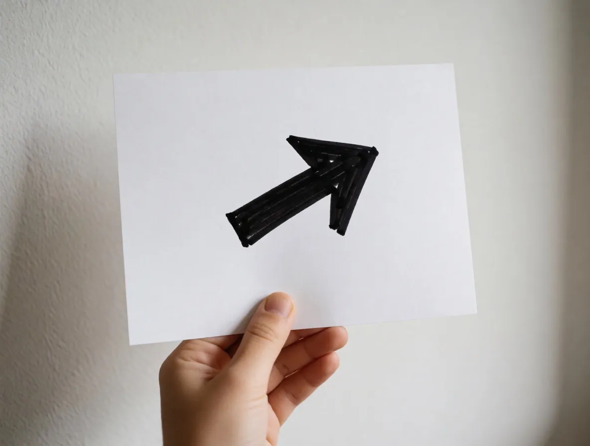 A photograph of a child’s hand holding a sheet of paper with one thick black arrow on it