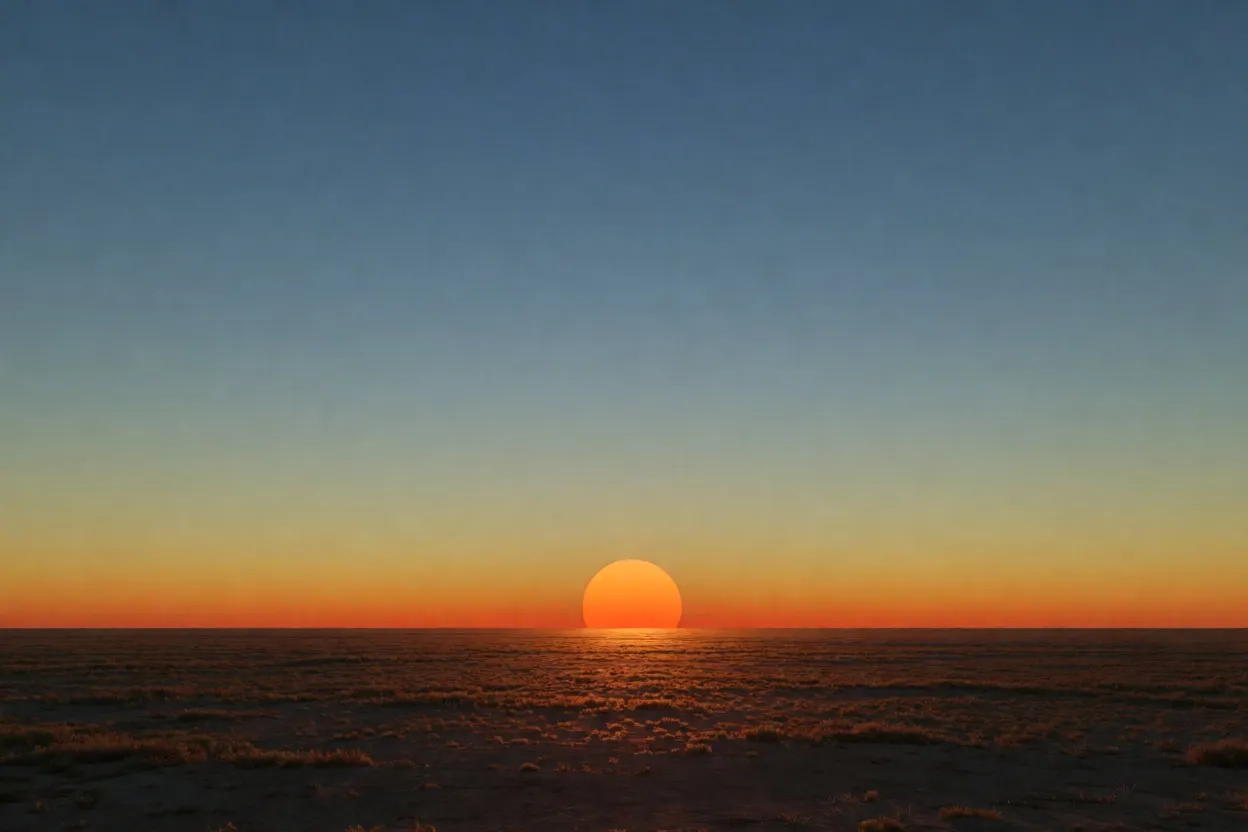 A photograph of a deep orange sun just above a flat horizon, the sky grading upward to deep blue